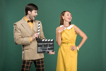 handsome man in vintage clothes holding film clapperboard while beautiful woman posing isolated on green