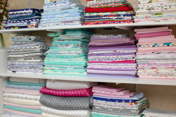 lots of bundles of different varieties of new fabric in many color collections kept on the shelf of a local store in Asia