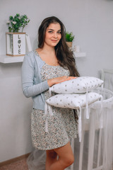 Young brown-haired girl with long hair smiling, holding grey . two pillows in her hands . Indoor. On the background the plate with the words love