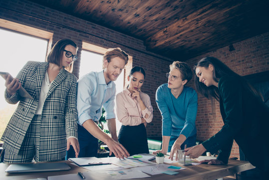 Close up photo stand around table business people she her he him his learn documents sheets papers talk tell speak development finance investment dressed formalwear jackets shirts spectacles specs