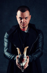 Brutal sorcerer guy holds in his hands a skull, on a dark background in the studio