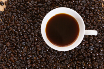 Cup of brewed espresso coffee on heap of dark coffee beans on wooden table.