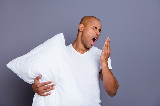 Close up photo unhealthy dark skin he him his macho bald head tired yawn yell scream shout hold pillow sleep and walk sleepless night wearing white t-shirt outfit clothes isolated grey background - Powered by Adobe