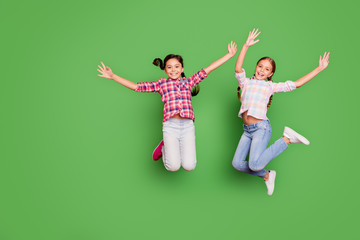 Full length body size photo two little age she her girls hand arm up jump high school competition cheerleaders wear casual jeans denim checkered plaid shirts isolated green vibrant vivid background