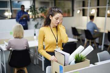 Frustrated young woman in yellow sweater standing at table and touching face with hand while...