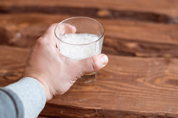 Male hand is holding a glass of beer on a wooden background.