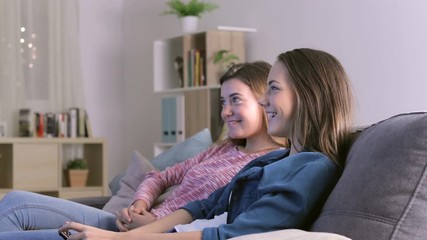 Two excited girls watching tv sitting on a couch at home in the night
