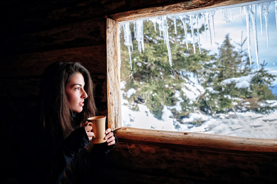 woman with a mug of tea looks out of the window in winter