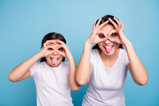 Close up photo beautiful two people brown haired mom little daughter best friends look through finger glasses specs okey symbol tongue out mouth wearing white t-shirts isolated bright blue background