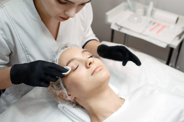 Beautician stand at client's head and cleaning skin on eyelids careful. Young woman lying on couch...