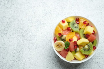 Tropical fruit salad in a white plate with sauce on a light background top view copy space