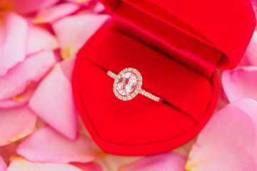 elegant wedding diamond ring in red heart jewelry box on beautiful pink rose petal background close up