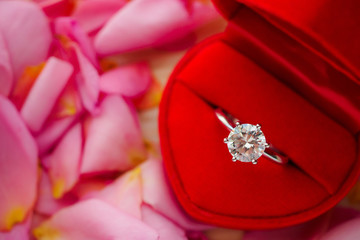 elegant wedding diamond ring in red heart jewelry box on beautiful pink rose petal background close up