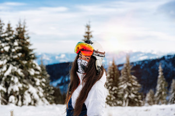 Girl with ski mask and snowboard on the background of snow-capped mountains enjoying a sunny winter...