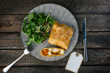 Strudel with pumpkin, feta cheese and vegetable salad, served on the ceramic plate with the cutlery.