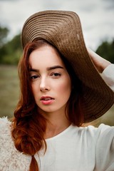 portrait of attractive young red haired woman in hat posing outdoors 