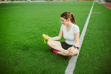 Theme sport and health. Beautiful young girl sitting resting on green grass, artificial turf...