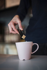 A waiter's hand in the cafe holds a piece of sugar in the pinchs that puts it in a cup of coffee or tea. cake and people in cafe concept.