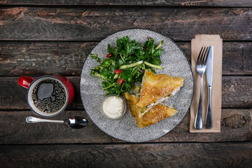 Strudel with chicken, zucchini and vegetable salad, served on the ceramic plate with the cutlery and the cup of coffee.