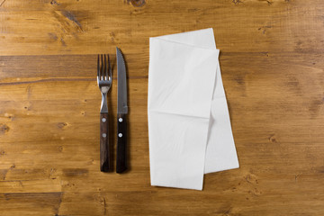 Cutlery and paper napkin on wooden background.