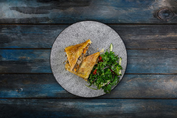 Strudel with stewed cabbage, meat and vegetable salad, served on the ceramic plate.