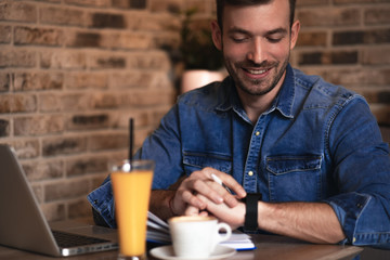 Young man sitting at cafe and working on laptop, casual businessman looking at smart watch.