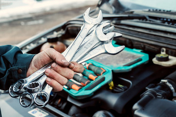 Mechanic repairs car. Wrenchs in male hand. Car service, engine repair, car repair shop.