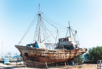 Old rusty fishing ship standing on land near sea.