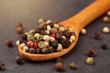 Macro shot of peppercorn mix in a wooden spoon on a dark stone kitchen board with sun haze light