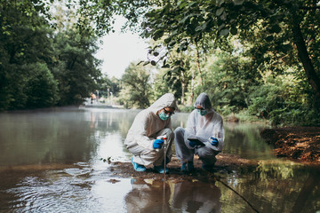 Two scientists in protective suits taking water samples from the river.