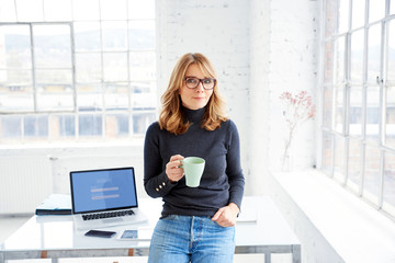 Beautiful businesswoman standing in the office while drinking her coffee