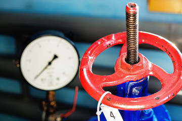 red valve and pressure sensor on the gas supply or heating pipe. Industrial background with...