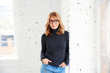 Portrait of attractive woman wearing roll neck sweater and jeans while looking at camera and smiling