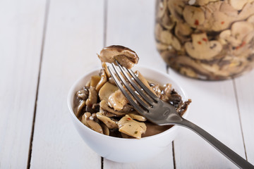 mushrooms in oil in ceramic bowl on white wooden background.