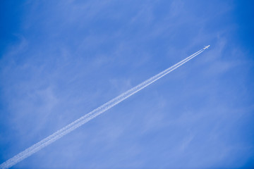 Plane flies in the sky leaving behind a strip