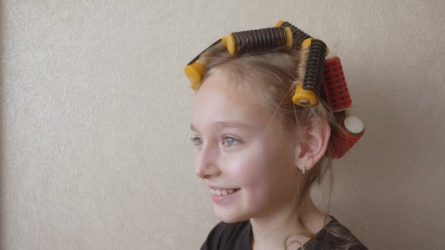 Portrait smiling young girl with curlers on hair on light wall background. Joyful girl teenager while curling hair on rollers on copy space background. Beauty and hairstyle. Girl show tonque copyspace