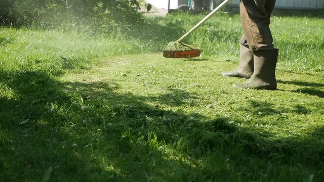 Male worker with petrol lawn mower trimmer with motor cutting grass on a sunny summer day. Cutting grass in the country. Slowmotion