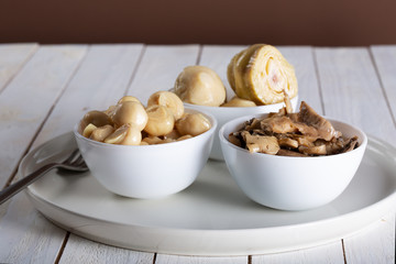 mushrooms and artichokes in oil in ceramic bowl on white wooden background.