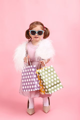 Beautiful little girl in fashion clothes with shopping bags on pink background