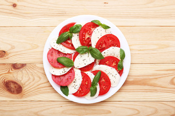 Mozzarella, tomatoes and basil leafs on brown wooden table