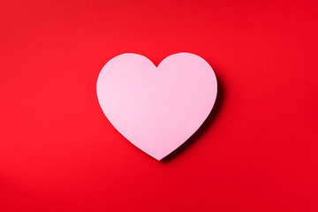 Pink heart cutted from paper over red background with copy space. Top view. Valentine's Day. Love, date, romantic concept.
