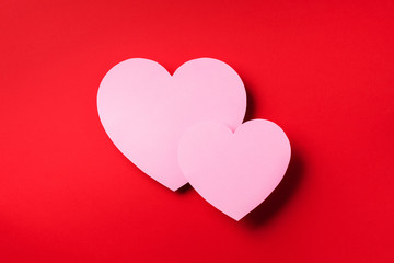Two pink hearts cutted from paper over red background with copy space. Top view. Valentine's Day. Love, date, romantic concept.