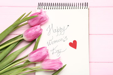 Text Happy Women's Day with pink tulip flowers on wooden table