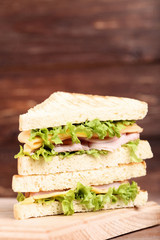 Tasty sandwiches with cutting board on brown wooden background
