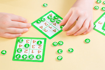Hands of a child playing sudoku board game filling the card with number tokens. Education concept...