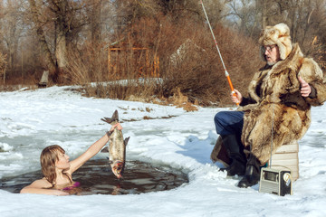 Young girl emerged from the ice-hole and stretches the fish to an elderly fisherman.