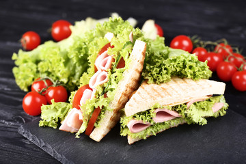 Sandwiches with ham, cheese and vegetables on black wooden table