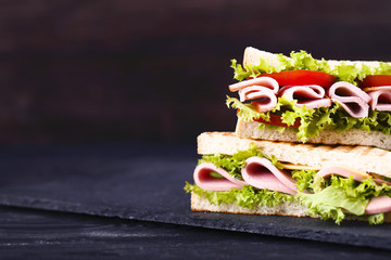 Sandwiches with ham, cheese and vegetables on black wooden table