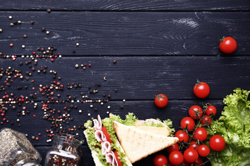 Tasty sandwiches with vegetables and pepper spices on black wooden table