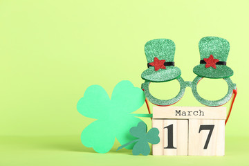 Paper clover leafs with wooden calendar and glasses on green background